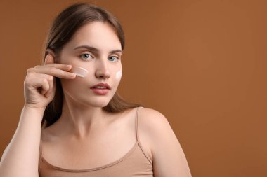 Kahverengi arka planda yüzüne krem süren güzel bir kadın. Metin için boşluk