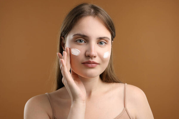 Красивая женщина со сливками на лице на коричневом фоне