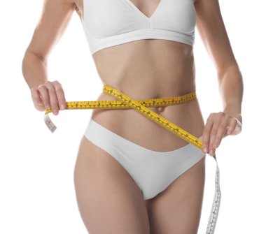 İnce vücutlu kadın, beyaz arka planda bel çevresini ölçüyor, yakın plan.