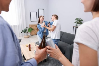 Genç kadın ve erkek evde karaoke yapıyor, seçici bir odak noktası var.