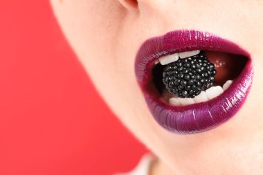 Dudak makyajı ve kırmızı arka planda böğürtlen olan güzel bir kadın, yakın plan. Metin için boşluk