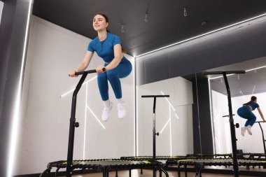Spor salonunda trambolinde zıplayan gülümseyen kadın, düşük açı.