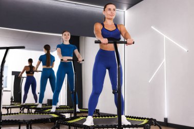 Spor salonundaki mini egzersiz trambolinlerinde, düşük açılı genç kadınlar.