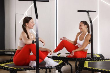 Spor salonundaki trambolinde konuşan gülümseyen kadınlar.