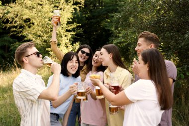 Bir grup mutlu arkadaş dışarıda bira bardaklarını tokuşturuyor.