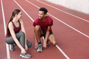 Stadyumda spor ayakkabılarının bağcıklarını bağlayan gülümseyen koşucular. Metin için boşluk