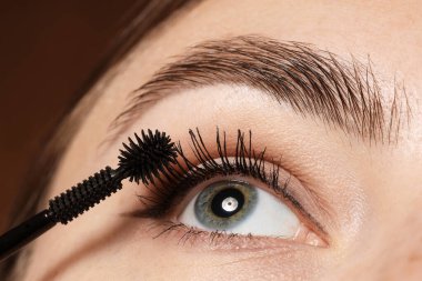 Kahverengi arka planda kirpiklerine rimel süren kadın, yakın plan.