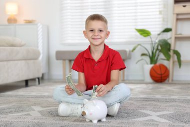 Küçük çocuk evdeki domuz kumbarasına cep harçlığı koyuyor.