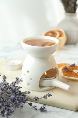 Aroma lambası, yanan mum, lavanta ve beyaz masada kuru portakal dilimleri, yakın plan.