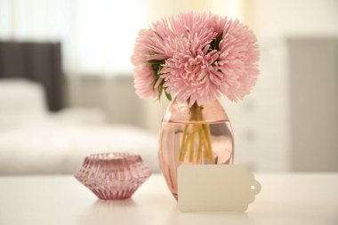 Boş kart, içinde çiçekler olan vazo ve beyaz masa üzerinde mum.