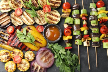 Vejetaryen barbeküsü. Lezzetli ızgara sebzeler, maydanoz ve sos siyah masada, düz yerde.