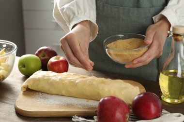 Kadın mutfaktaki ahşap masada çiğ elmalı turtanın üzerine kahverengi şeker serpiyor.