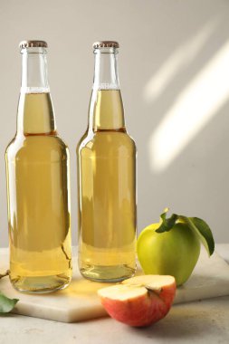 Cam şişelerde nefis elma şarabı ve gri masada hafif arka planda elmalar.