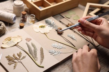 Ahşap masadaki kuru çiçekleri deftere koyan kadın, yakın plan.