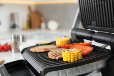 Electric grill with tasty meat and vegetables on table in kitchen, closeup