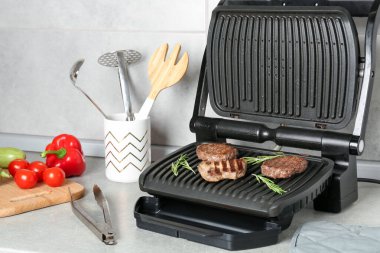 Biftek, pirzola, biberiye, sebze ve tencere ile açık elektrikli ızgara açık gri masa, yakın çekim