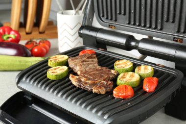 Biftek, kabak ve domatesle açık elektrikli ızgara açık gri masa, yakın plan.