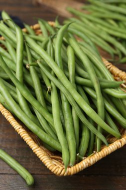 Hasır sepetin içindeki taze yeşil fasulye kabukları ahşap masanın üzerinde, yakın plan.