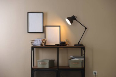 Stylish lamp, other decor and books on console table near beige wall indoors