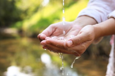 Su kavramını sakla. Nehrin kenarında ellerini temiz suyun altında tutan kadın, yakın plan.