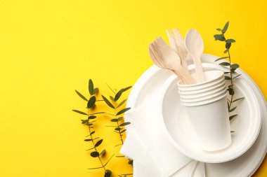 Sarı arka planda tek kullanımlık sofra takımı ve okaliptüs dalları. Metin için boşluk