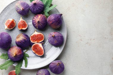 Taze incir ve yeşil yapraklar gri desenli masada, düz yerde. Metin için boşluk