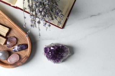 Farklı güzel değerli taşlar, kitap ve lavanta çiçekleri beyaz mermer masada, düz yerde. Metin için boşluk