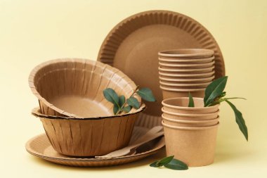 Bej arkaplanda tek kullanımlık eşyalar ve yeşil yapraklar, yakın plan