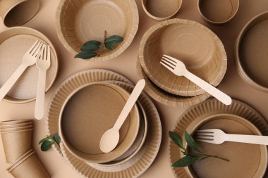 Koyu bej arkaplanda tek kullanımlık eşyalar ve yeşil yapraklar var.