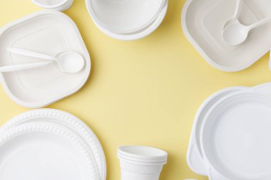Soluk sarı arka planda tek kullanımlık plastik sofra takımından yapılmış çerçeve düz. Metin için boşluk