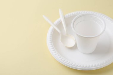 Soluk sarı arka planda tek kullanımlık plastik sofra takımı, yakın plan. Metin için boşluk