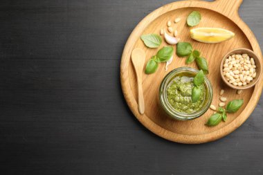 Kavanozda taze pesto sosu, siyah ahşap masada kaşık ve malzemeler, üst manzara. Metin için boşluk
