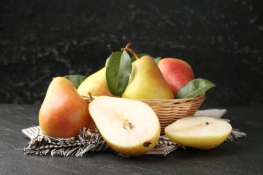 Siyah masadaki hasır kasede taze armut ve yapraklar, yakın plan.