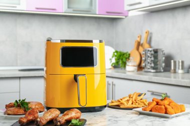 Modern air fryer and cooked meals on white marble table in kitchen