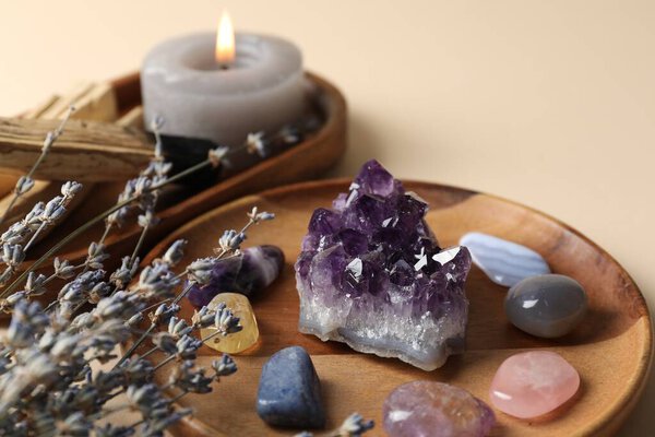 Различные красивые драгоценные камни, лаванда, палочки Пало Санто и горящая свеча на бежевом фоне, крупным планом