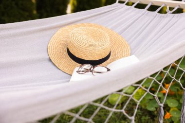 Hasır şapka, gözlük ve açık hava hamağı kitabı.