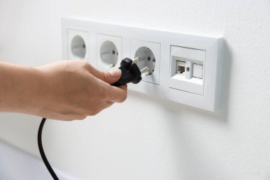Kadın prizi beyaz duvara takıyor, yakın plan.
