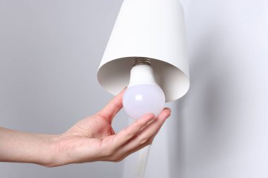 Evdeki gri duvarın yanında ampulü değiştiren kadın, yakın plan.