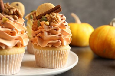 Renkli kremalı, tarçınlı, fındıklı ve sonbahar dekorlu lezzetli kekler gri masada, yakın plan.