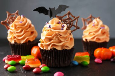 Yarasa tepeli lezzetli kapkekler, çikolata ağı ve koyu dokulu masalarda gri arka planda renkli şekerler, yakın plan. Cadılar Bayramı