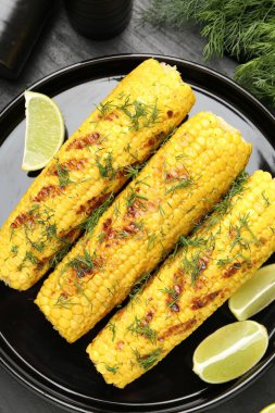 Lezzetli ızgara mısır koçanları, dereotu ve limon dilimleri siyah masada, düz yerde.