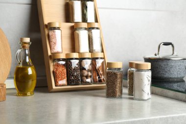 Cam kavanozlarda farklı baharatlar ve mutfakta açık gri masada yağlar.