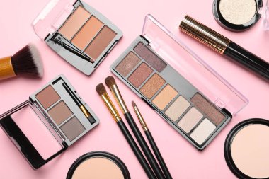 Flat lay composition with colorful eyeshadow palettes, powders and makeup brushes on pink background