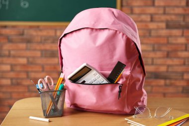 Sınıftaki masasında farklı kırtasiye malzemesi olan pembe bir sırt çantası.