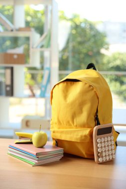 Sırt çantası, farklı kırtasiye malzemeleri ve sınıfta masanın üzerinde elma.