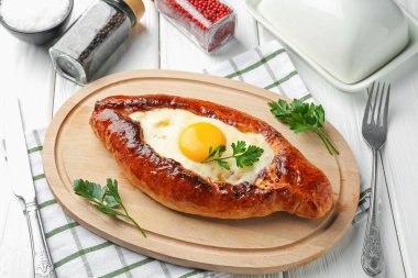 Beyaz ahşap masada servis edilen peynirli ve yumurtalı lezzetli khachapuri.