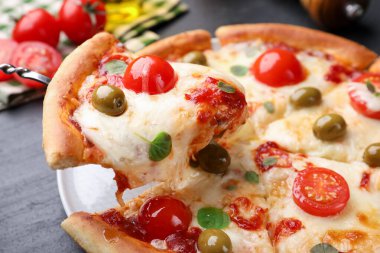 Peynirli, domatesli ve zeytinli lezzetli pizzayı koyu gri masada yakın plan çekiyoruz.