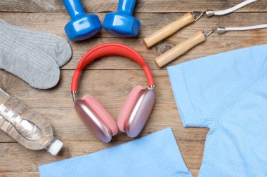 Spor kıyafetleri, spor malzemeleri ve ahşap arka planda kulaklıklar, düz yatış.