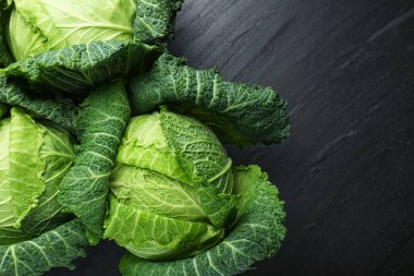 Fresh Savoy cabbages on black textured table, flat lay. Space for text