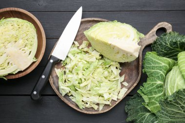 Cut fresh Savoy cabbages and knife on black wooden table, flat lay